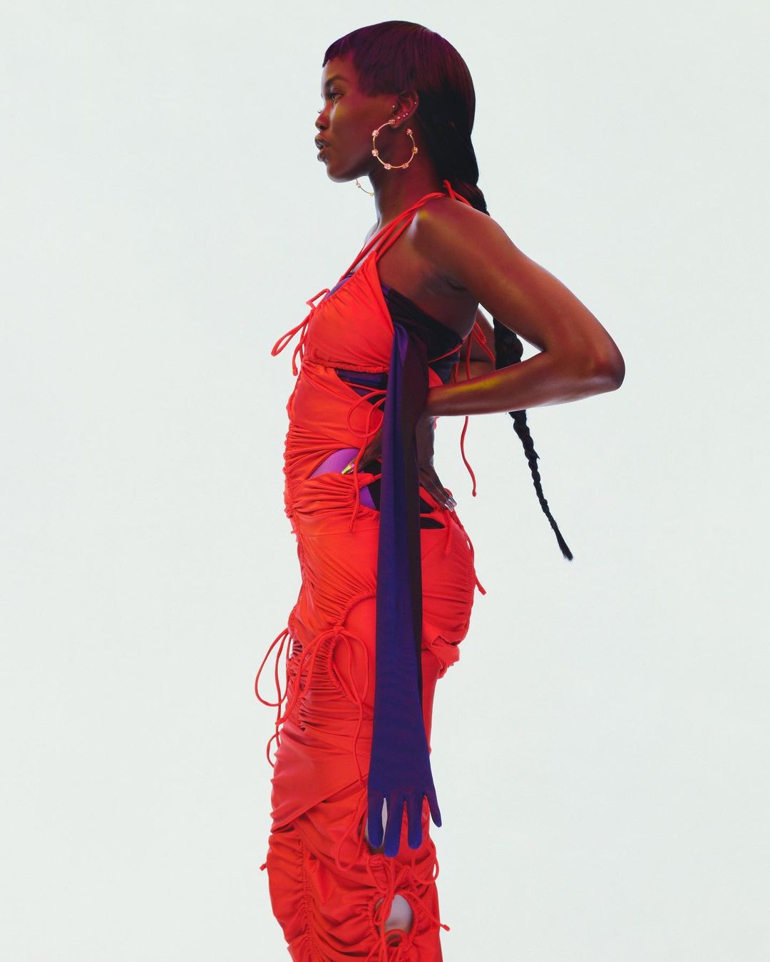 Side profile studio shot of a Black woman in a red ruched dress with a blue opera glove, against a white backdrop, fashion photography.