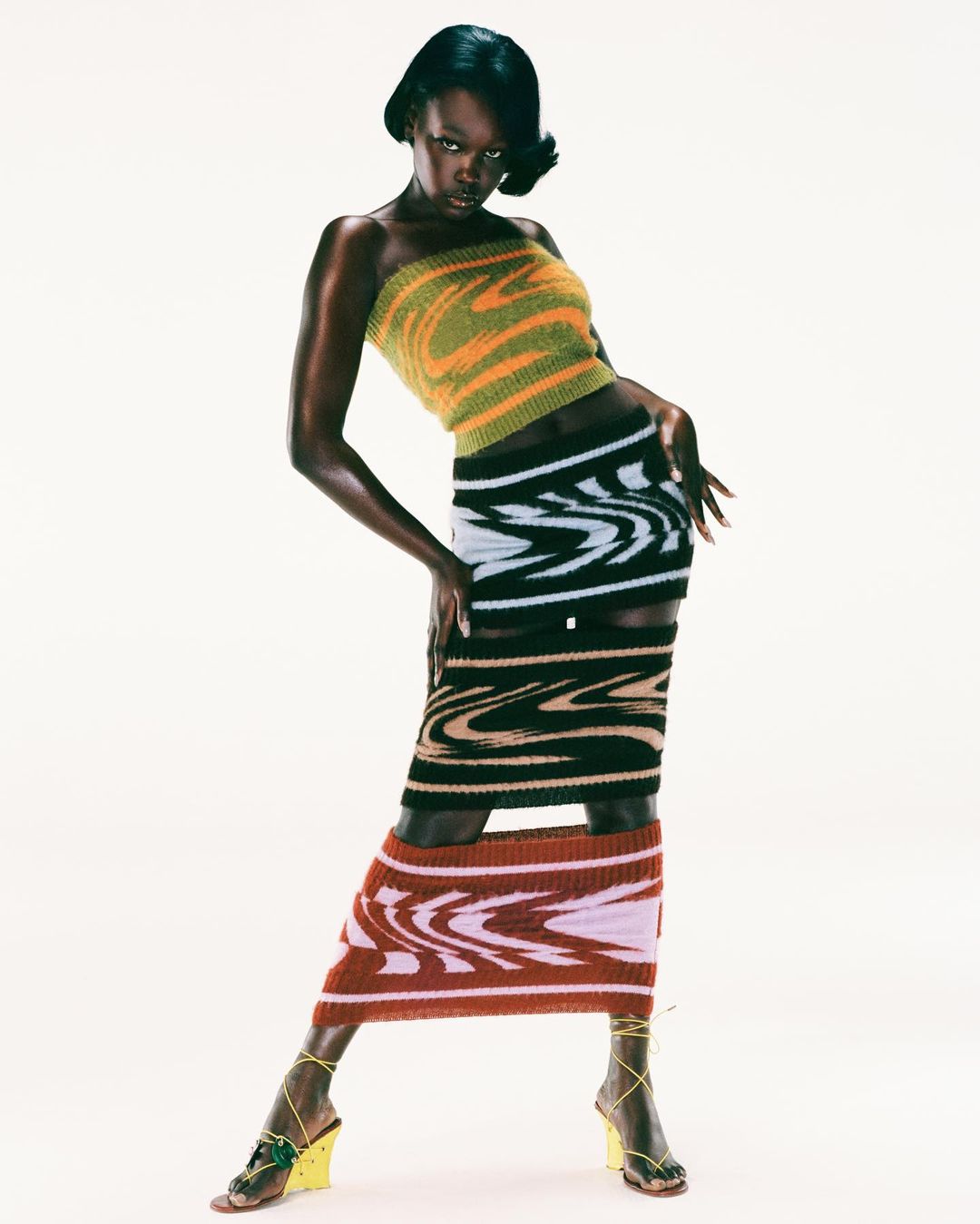 Black woman in striped knit bandeau top and matching skirts posing against a plain white background by Arnaud Lajeunie