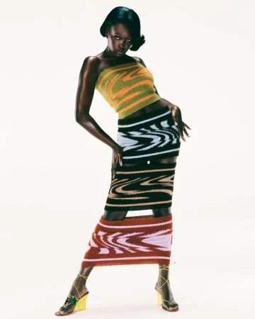 Black woman in striped knit bandeau top and matching skirts posing against a plain white background by Arnaud Lajeunie