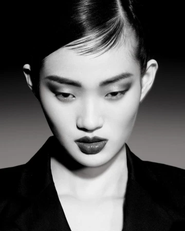 Close-up black and white portrait of an East Asian woman wearing a dark blazer against a grey seamless background