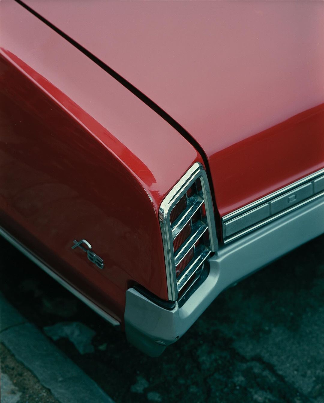 Close-up of the rear of a red vintage car with chrome detailing, including the bumper and tail lights, parked near a concrete curb.