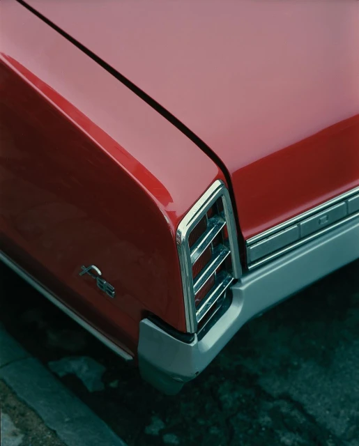 Close-up of the rear of a red vintage car with chrome detailing, including the bumper and tail lights, parked near a concrete curb.