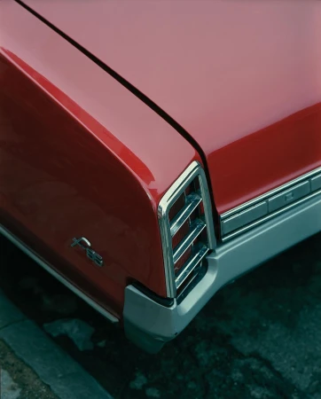 Close-up of the rear of a red vintage car with chrome detailing, including the bumper and tail lights, parked near a concrete curb.