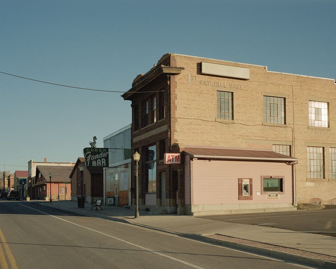 Small town main street with brick buildings under a clear blue sky, showcasing vintage architecture and an ATM on the corner.