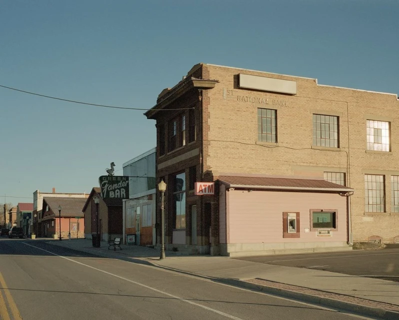 Small town main street with brick buildings under a clear blue sky, showcasing vintage architecture and an ATM on the corner.