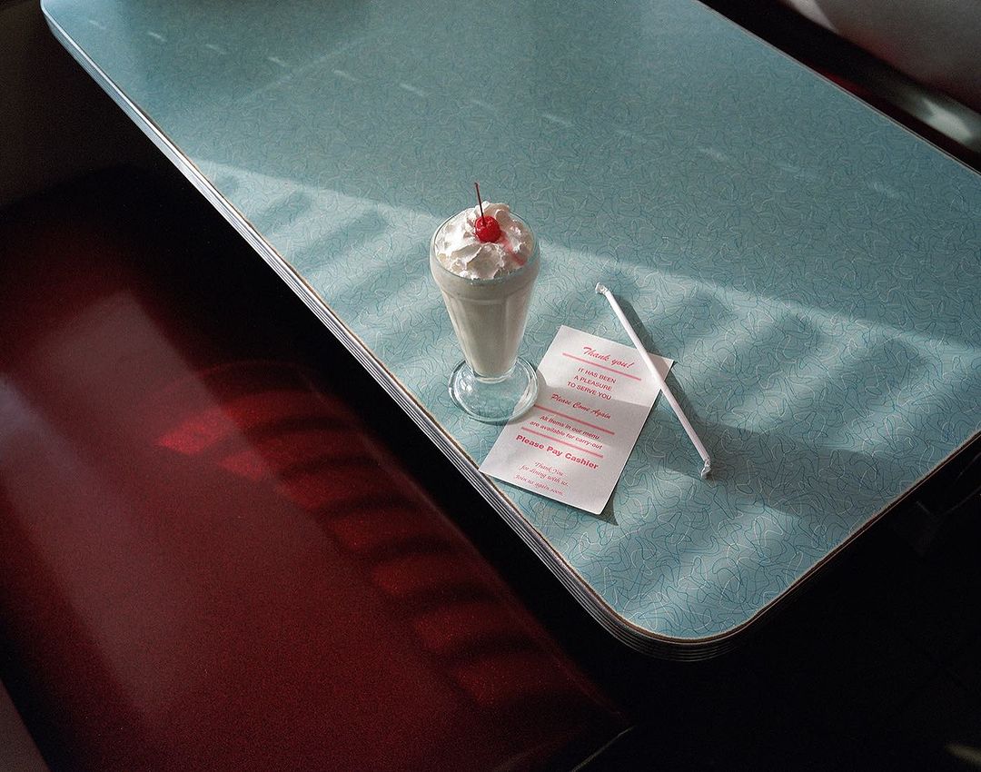 Milkshake with whipped cream and cherry on a diner table, accompanied by a straw and a thank you note in a vintage setting.
