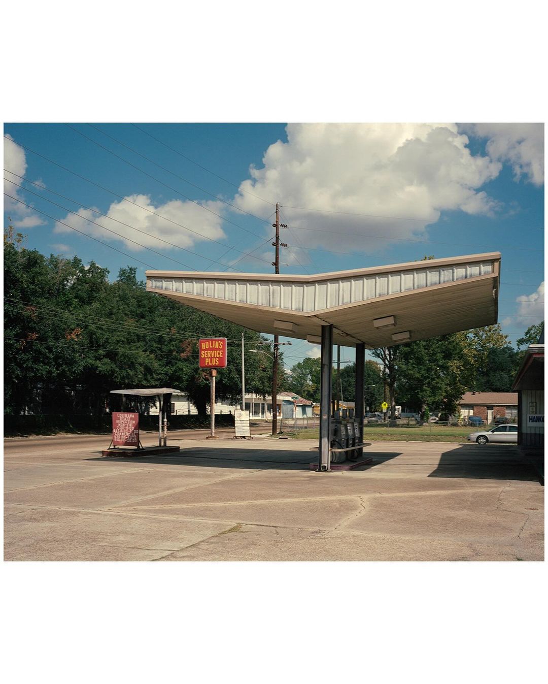 An empty vintage gas station with a large canopy, set against a backdrop of blue sky and trees, under the bright daylight.