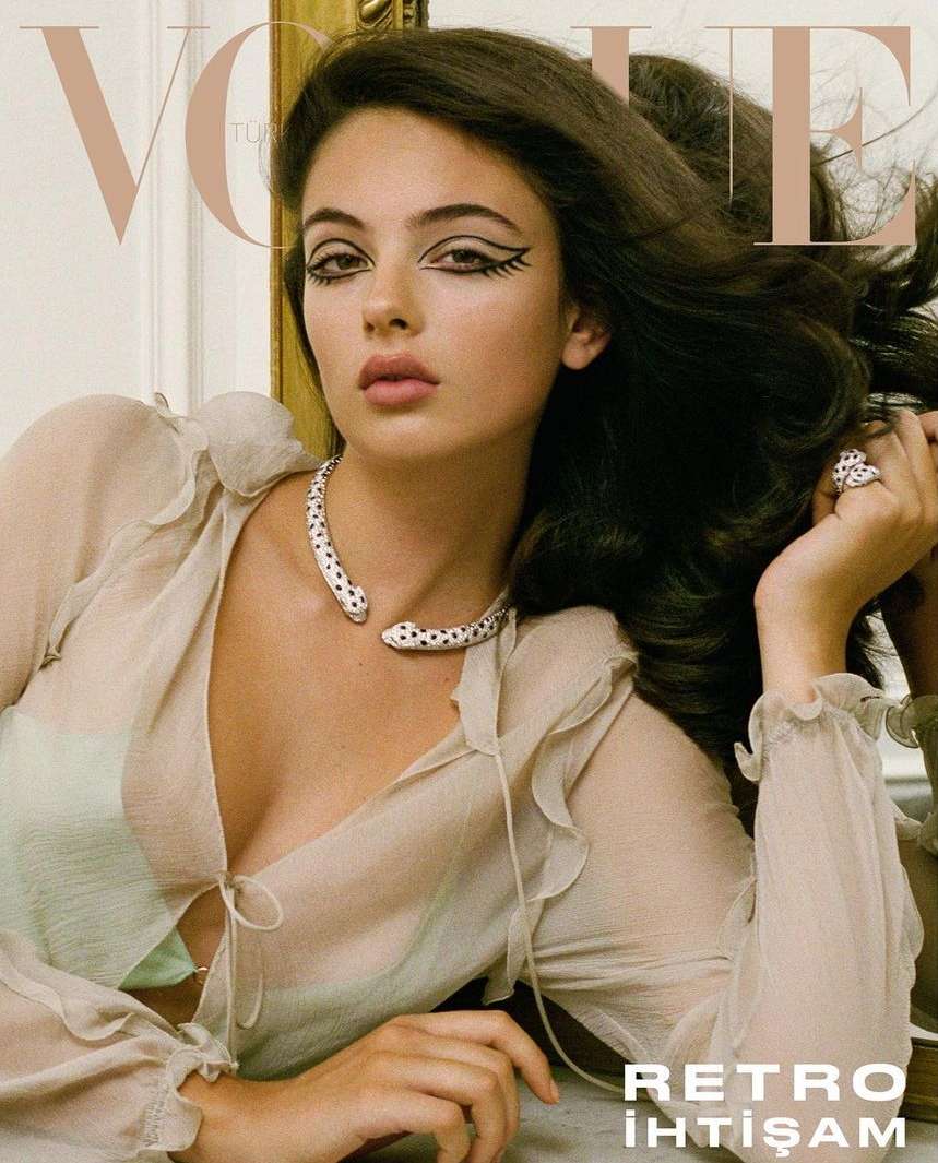 Vogue magazine cover featuring a woman with dark hair and graphic eyeliner, wearing a sheer top and statement jewelry, against a neutral backdrop.