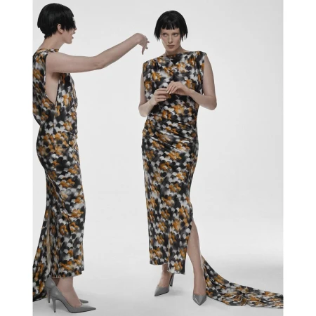 Two women pose in patterned dresses in a white studio. One model stands while the other reaches out, both wearing floor-length dresses.