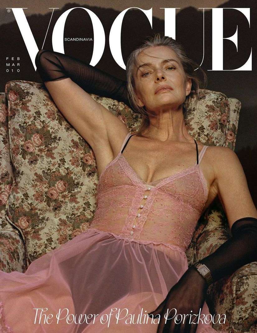 Vogue cover featuring a mature woman reclining in a floral chair, wearing a sheer pink dress and black gloves against a blurred background.
