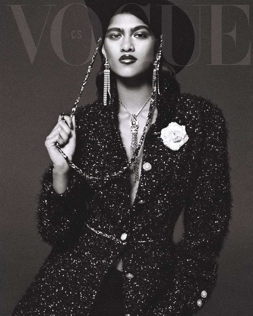 Vogue cover featuring a female model in a black hat and tweed jacket with statement jewelry, posing in a studio setting.