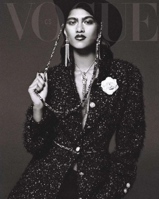 Vogue cover featuring a female model in a black hat and tweed jacket with statement jewelry, posing in a studio setting.