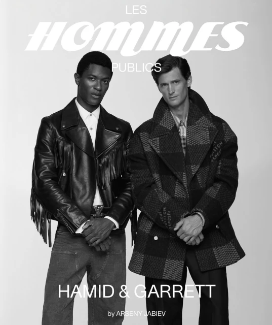 Monochrome fashion shot featuring two male models in stylish jackets, one leather fringe and one checkered, against a light backdrop.