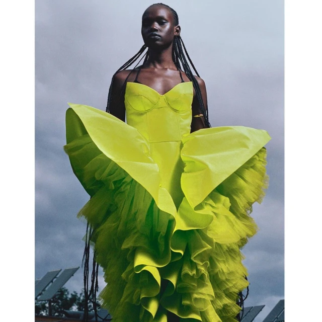 A striking portrait of a Black woman in a voluminous neon yellow gown against a cloudy sky, showcasing fashion and editorial photography.