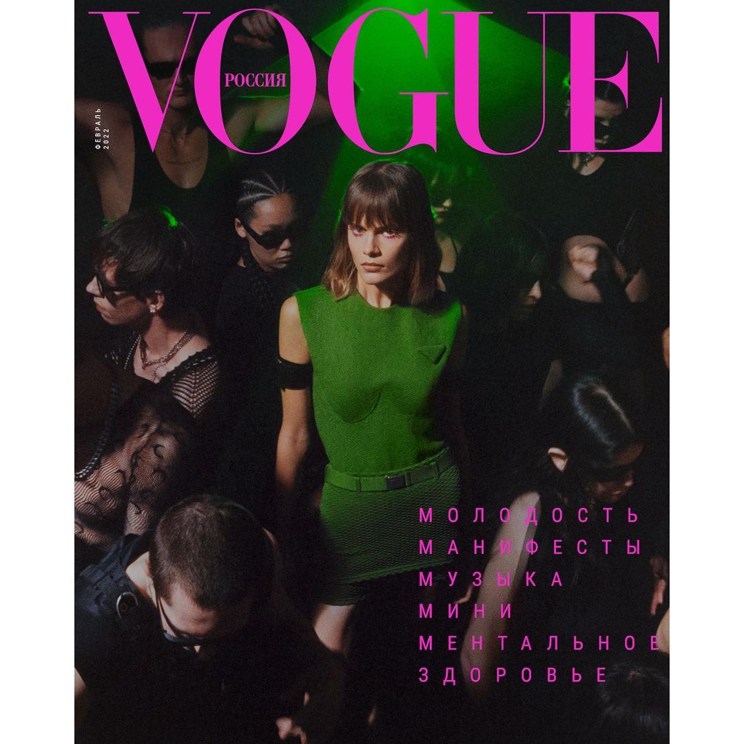 Vogue Russia cover featuring a female model in a green dress surrounded by a diverse group of people in a dark, club-like setting.