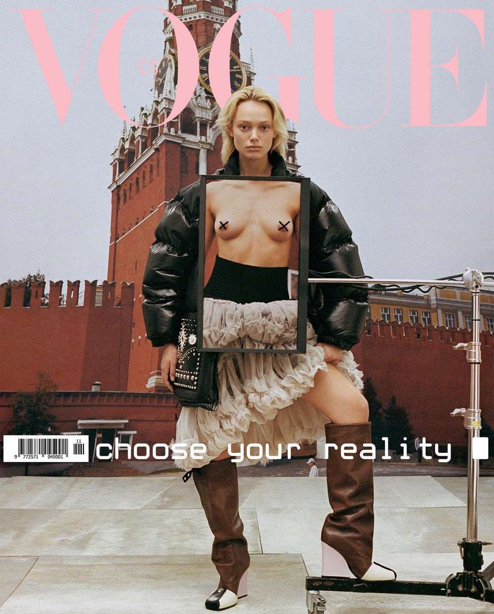 Vogue cover featuring a blonde model in a black jacket, white skirt, and thigh-high boots, posing against a red brick building backdrop.