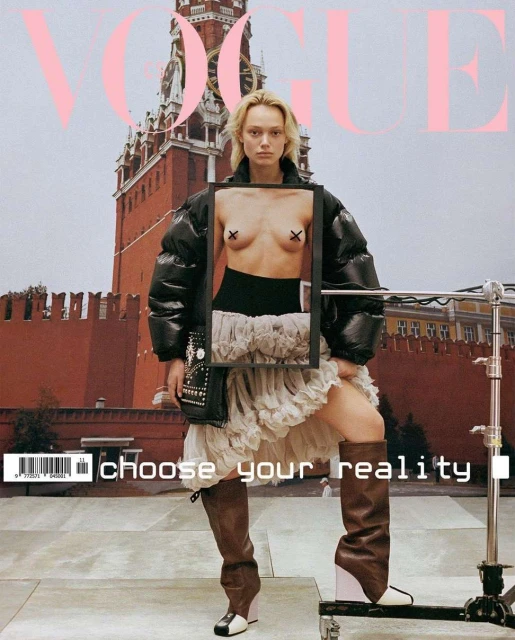Vogue cover featuring a blonde model in a black jacket, white skirt, and thigh-high boots, posing against a red brick building backdrop.