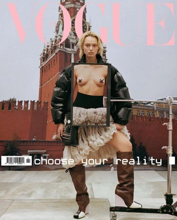 Vogue cover featuring a blonde model in a black jacket, white skirt, and thigh-high boots, posing against a red brick building backdrop.