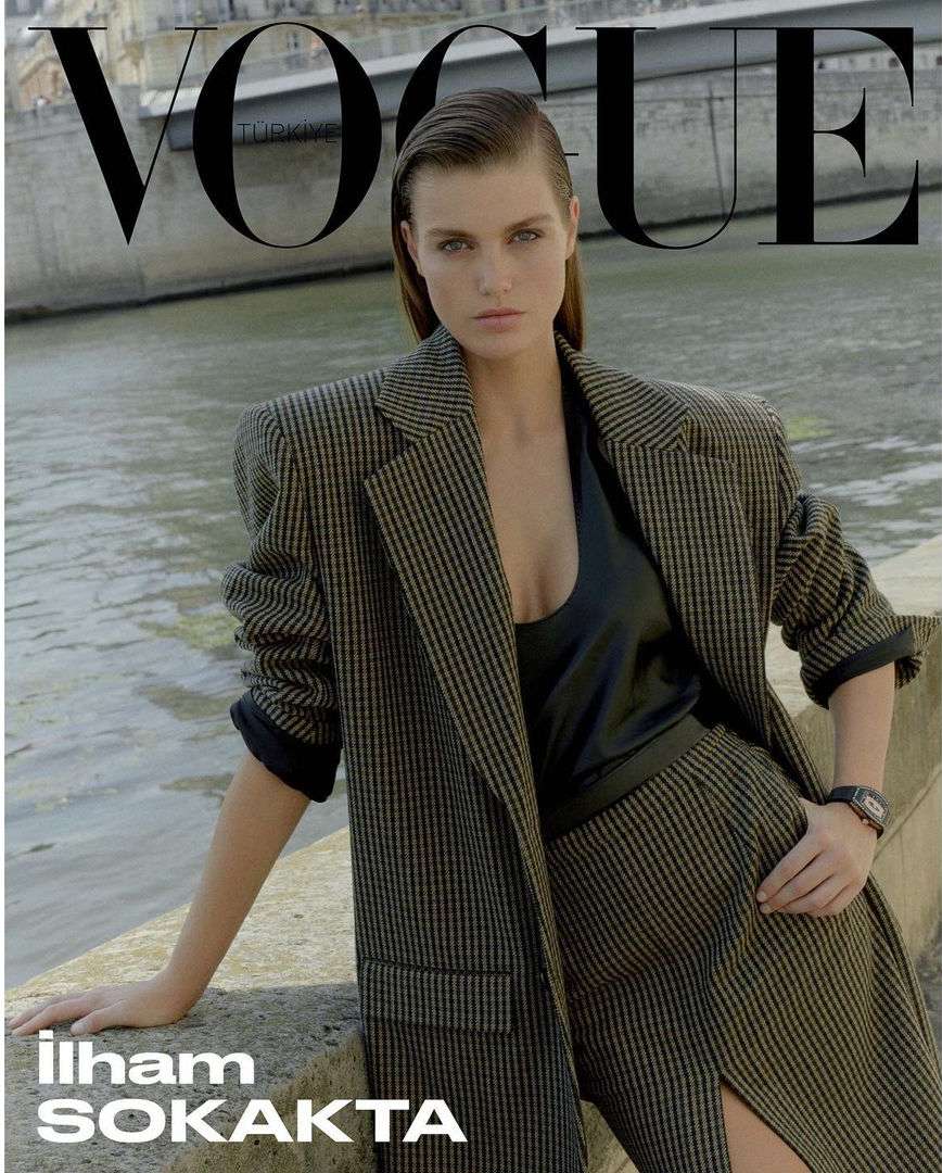 Vogue cover featuring a model in a pinstripe skirt suit, posed in front of a river and architectural background under soft light.