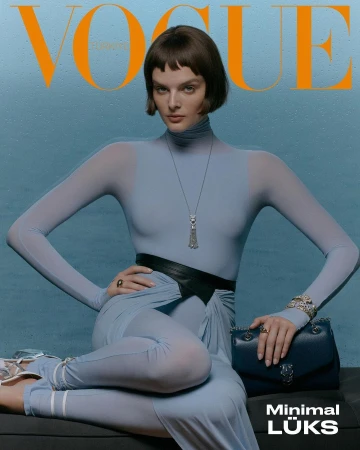 Vogue magazine cover featuring a woman in a light blue bodysuit, posing with a purse against a matching backdrop, striking a confident pose.