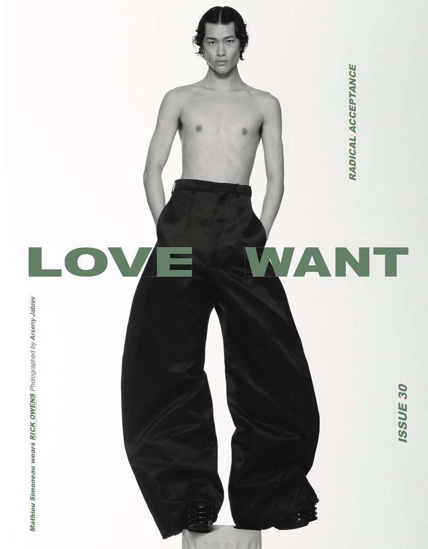 A shirtless male model poses against a white background wearing oversized black pants, showcasing a fashion editorial style.