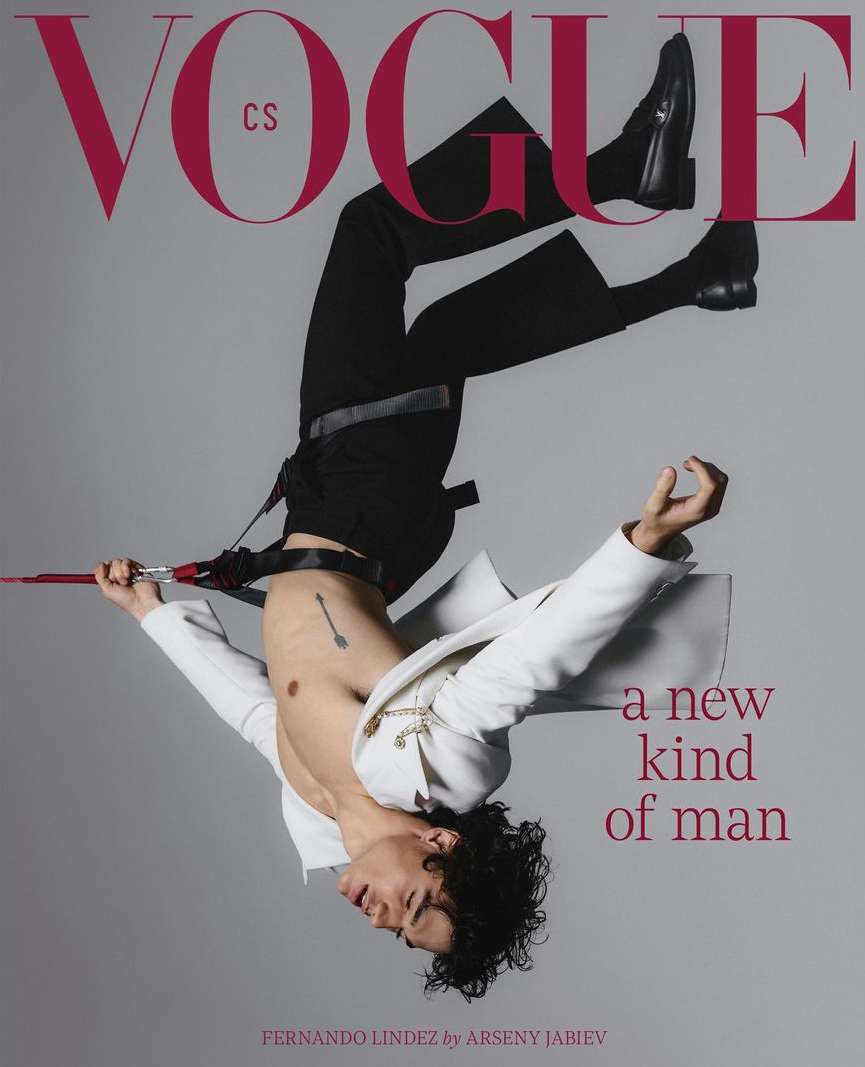 Vogue cover features a male model in black pants and boots, wearing a white jacket, in an upside-down pose against a grey backdrop.