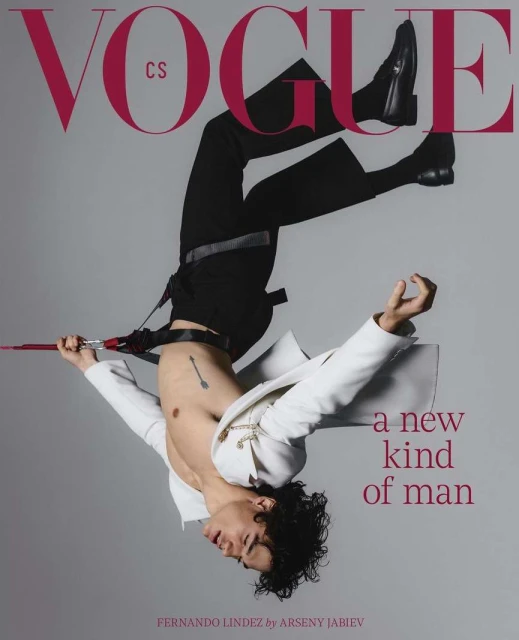 Vogue cover features a male model in black pants and boots, wearing a white jacket, in an upside-down pose against a grey backdrop.