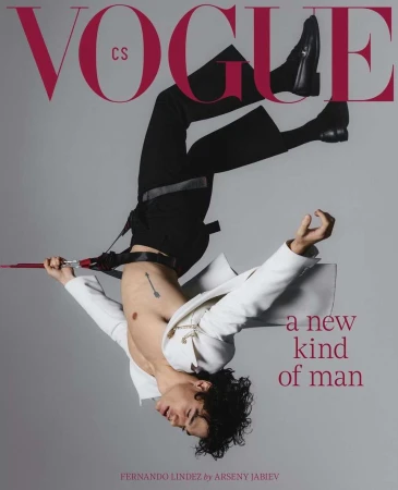 Vogue cover features a male model in black pants and boots, wearing a white jacket, in an upside-down pose against a grey backdrop.
