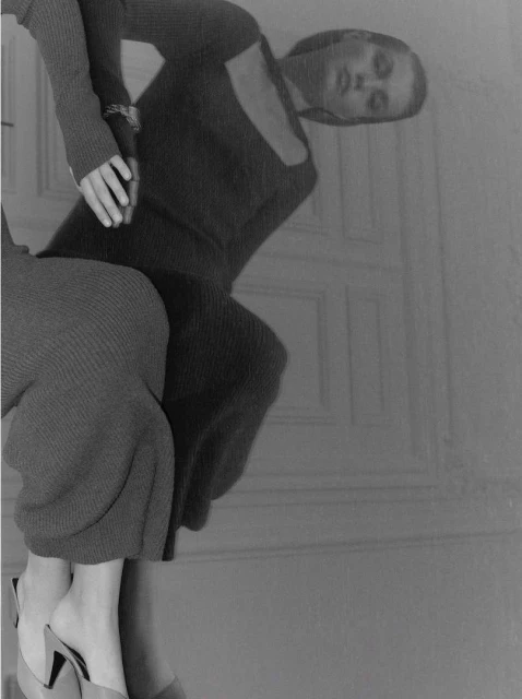 Two fashion models pose indoors wearing long sleeve knit dresses and heels in a black and white editorial fashion shot.