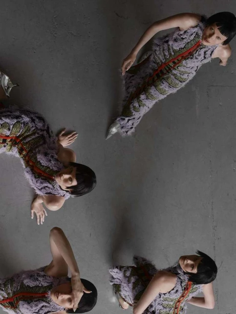 Four mirrored images of a woman in a patterned dress with a stern expression against a gray backdrop in a fashion editorial shoot.