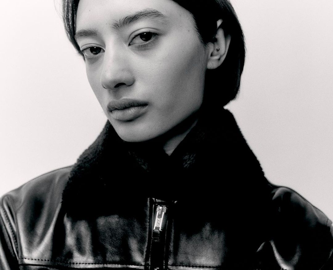 Monochrome portrait of an East Asian adult female wearing a black leather jacket, set against a plain white background in a studio.
