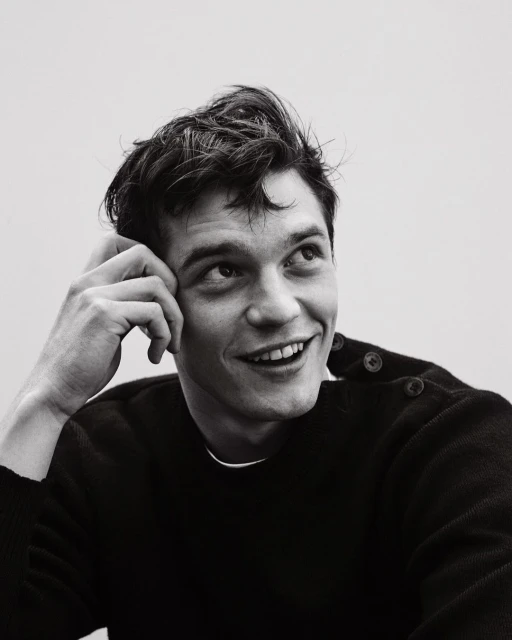 Monochrome portrait of smiling adult male with dark hair, head resting on hand, wearing a crewneck sweater and looking upward.