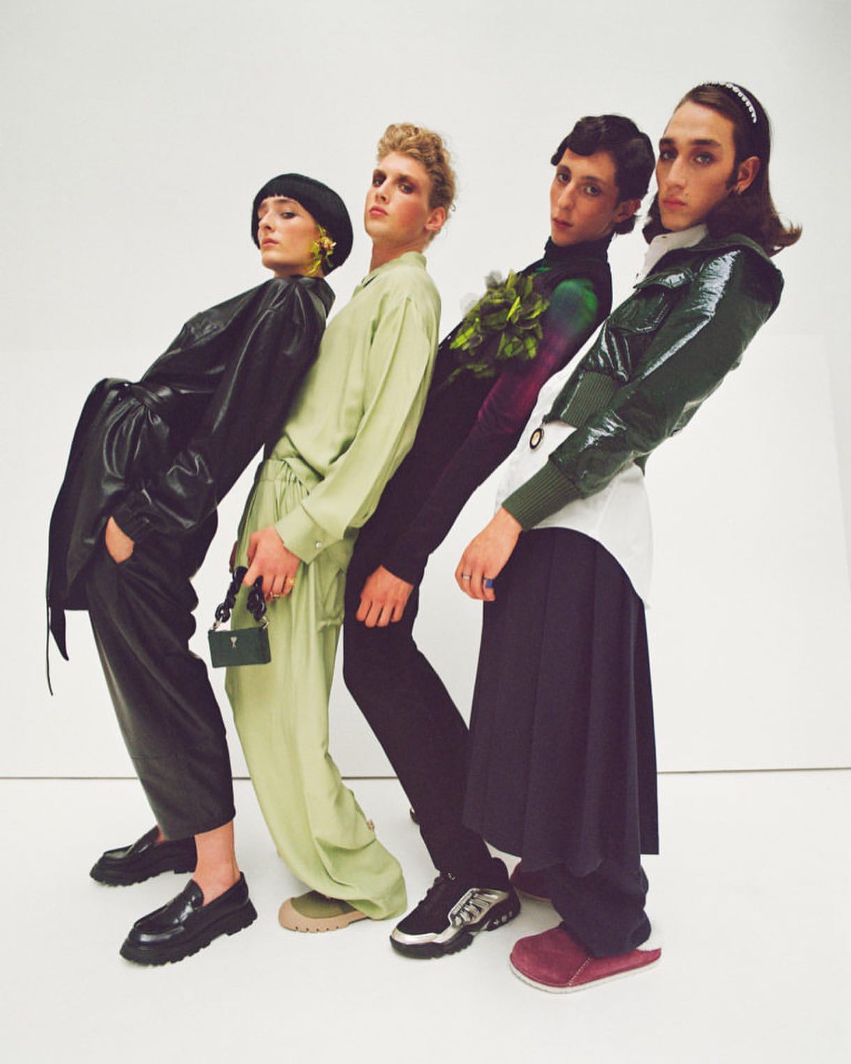 Fashion editorial shot with four people in different colored outfits posing in front of a white background in a studio environment.