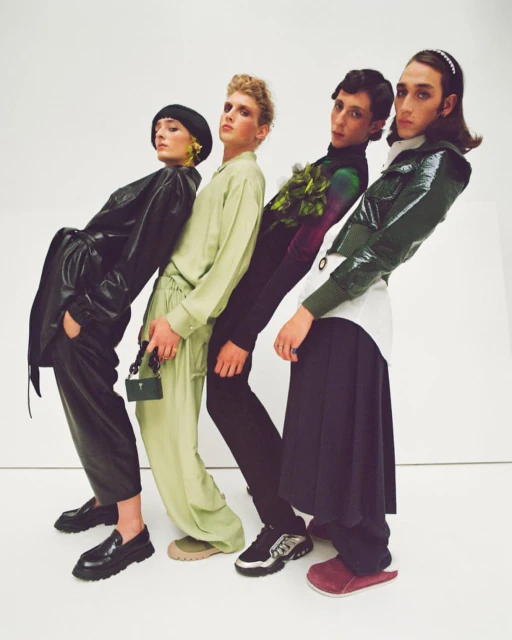Fashion editorial shot with four people in different colored outfits posing in front of a white background in a studio environment.