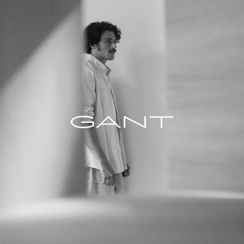 Man with curly hair and a mustache wearing a button-down shirt framed between structural architecture with overlayed text