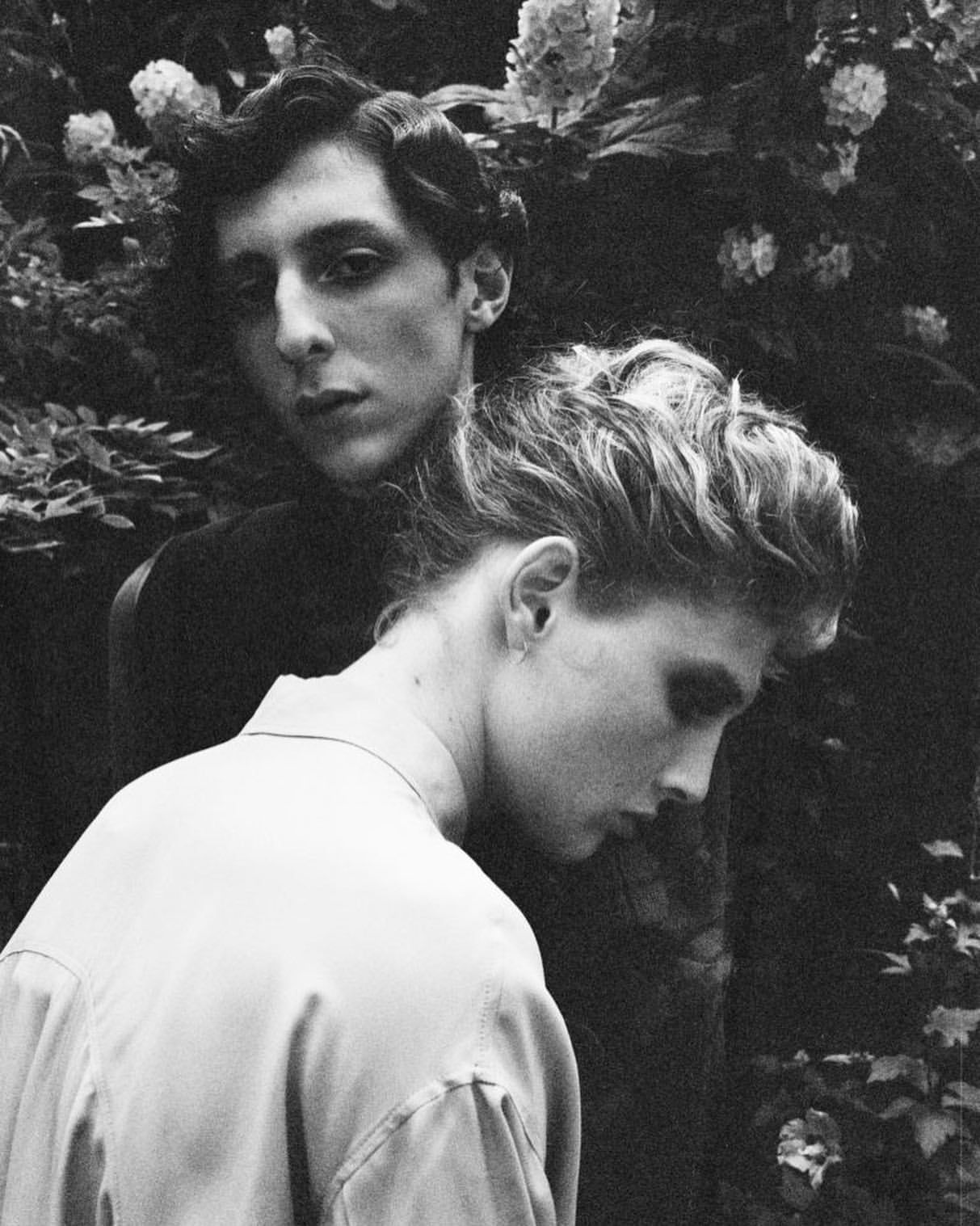 Black and white portrait of a man and woman posing closely outdoors amidst dense foliage in Paris by Arthur Delloye.