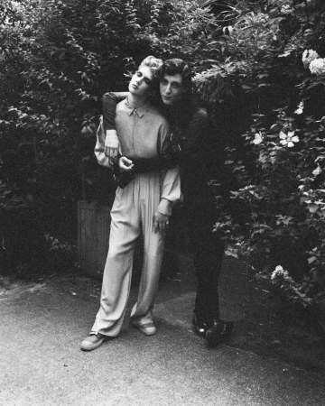 Two people posing together in a lush garden setting, photographed in black and white by Arthur Delloye in Paris.
