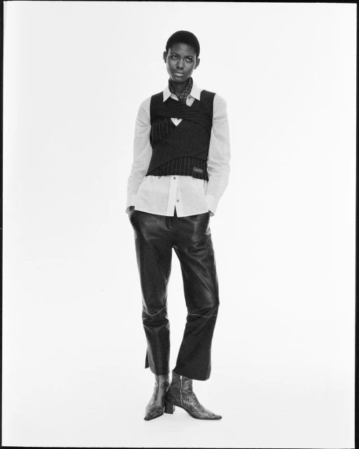 A fashion shot features a single Black female adult in a white button-down shirt, vest, leather trousers, and heeled boots against a white backdrop.