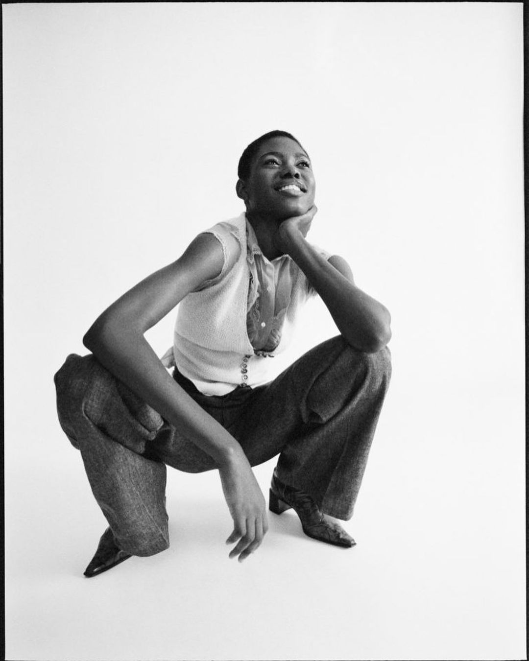Black and white portrait of an adult woman in an expressive pose, wearing casual clothing in a photo studio setting with a bright white backdrop.
