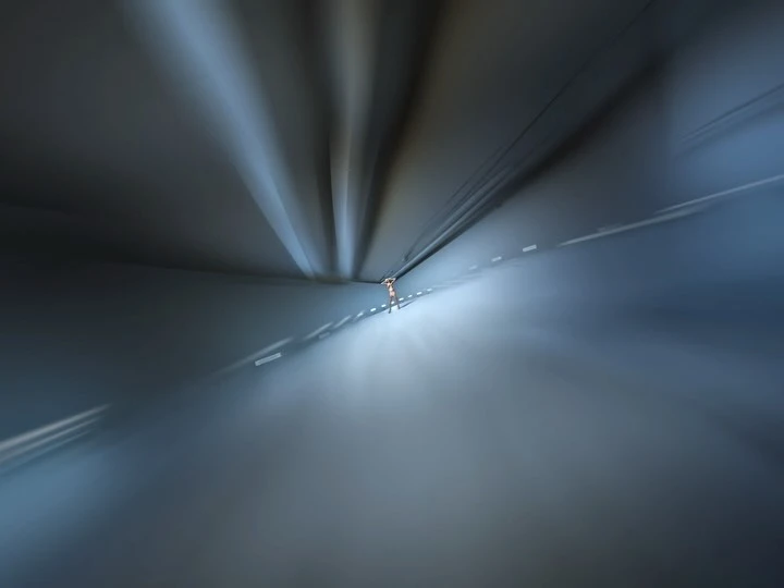 Abstract blurred road with central figure under bridge or tunnel, creating motion effect with converging lines and cool color palette.