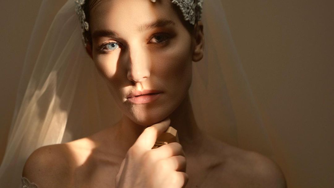 Close-up studio shot of a Caucasian woman with fair skin, wearing a veil and light makeup, with warm, even lighting highlighting her features.