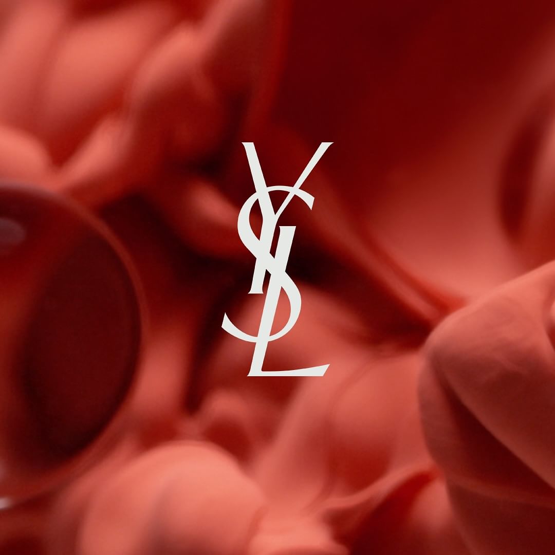 Yves Saint Laurent (YSL) logo in white against a blurry coral background with soft gradations and a luminous, cosmetic-like aesthetic.