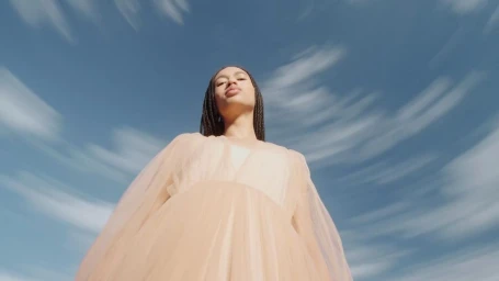 Low angle portrait of a woman in a sheer peach dress against a swirling blue sky by Arthur Valverde