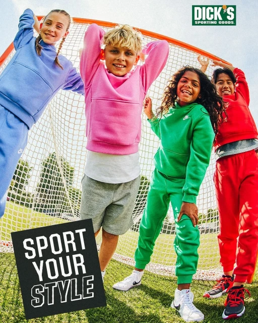 Group of four smiling children in colorful athleisure clothing, posed in front of a net and grassy field, Dick's Sporting Goods advertisement.