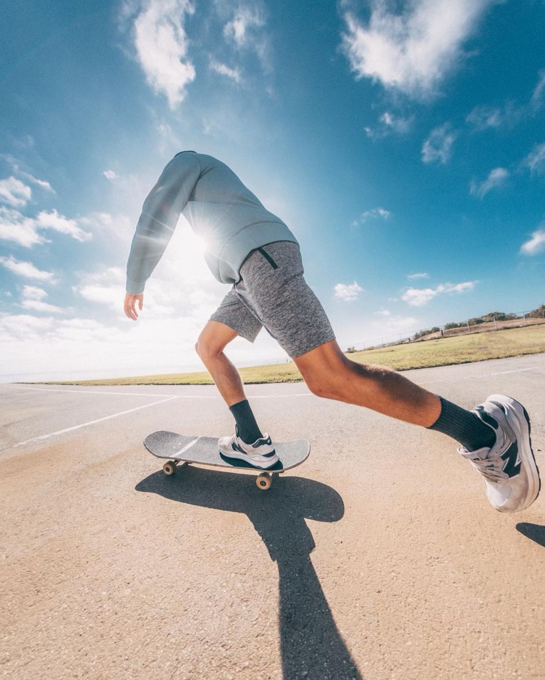 Athletic man in motion skateboarding on a paved road under a sunny sky. He wears athletic shorts and running shoes for sport lifestyle.