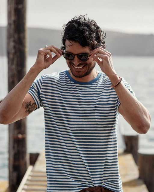Portrait of a smiling man in sunglasses, wearing a striped shirt, outdoors on a dock with a body of water in the background.