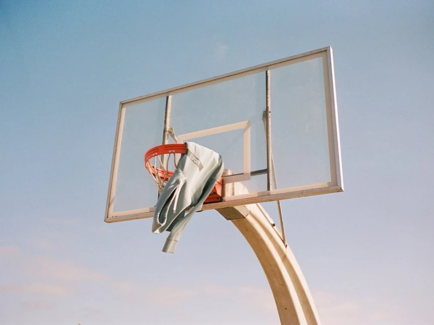 Outdoor shot of a basketball hoop with a jacket draped over the orange net against a bright blue daytime sky.