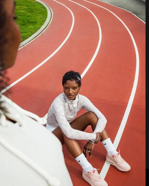 Woman in athletic wear sitting on red running track with green grass in the background, smiling. Outdoor fitness and athletics concept.