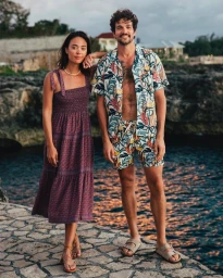 Man and woman standing together outdoors on a stone patio near water, wearing patterned resort wear.