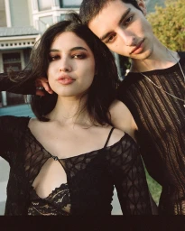 Portrait of a young woman and man leaning close together outdoors wearing black textured tops